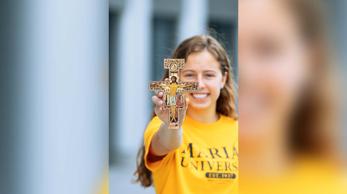 A student wearing a Marian University t-shirt holds up a decorative cross.