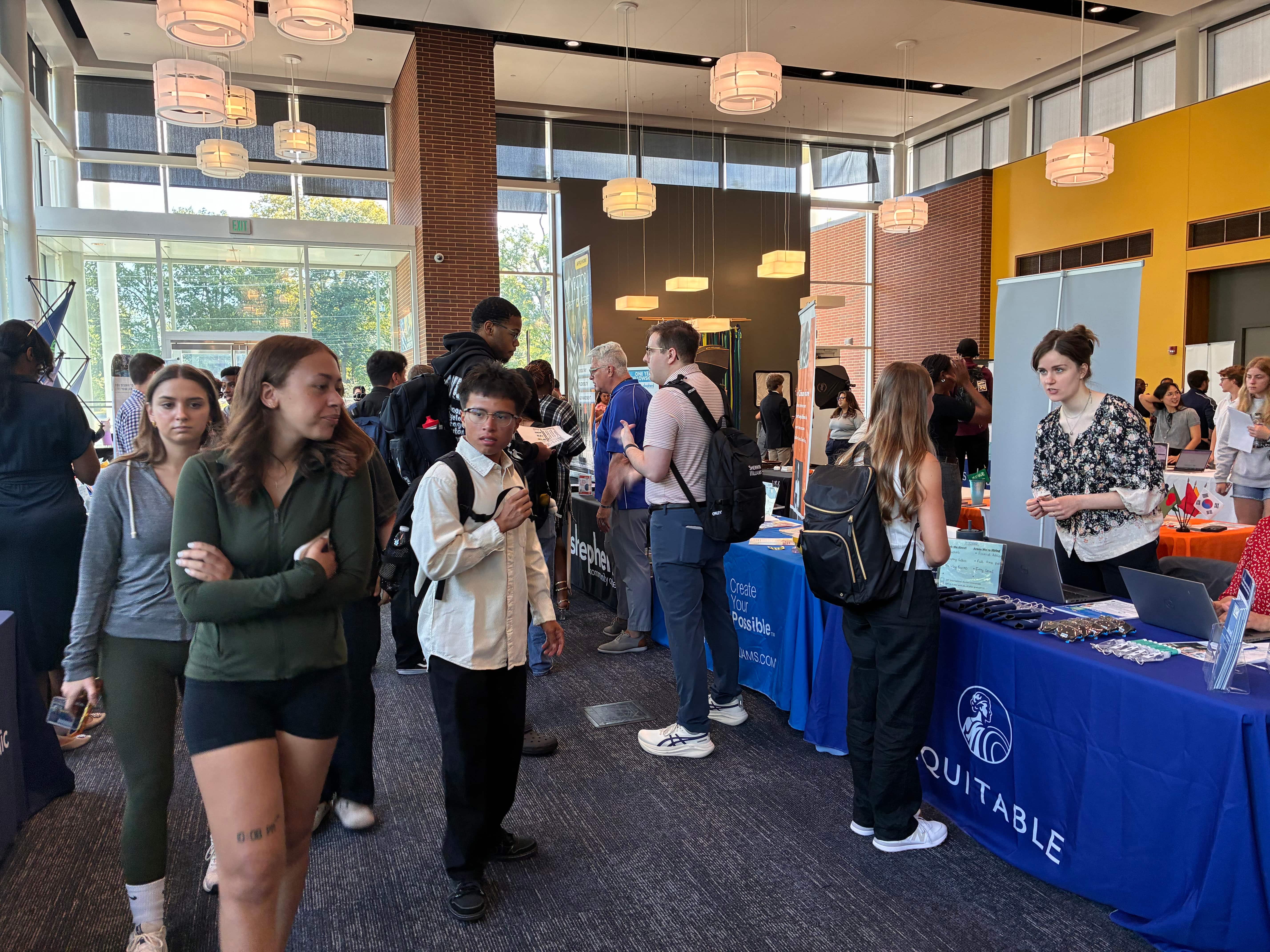 A bustling college fair showcasing various booths with attendees interacting and gathering information.