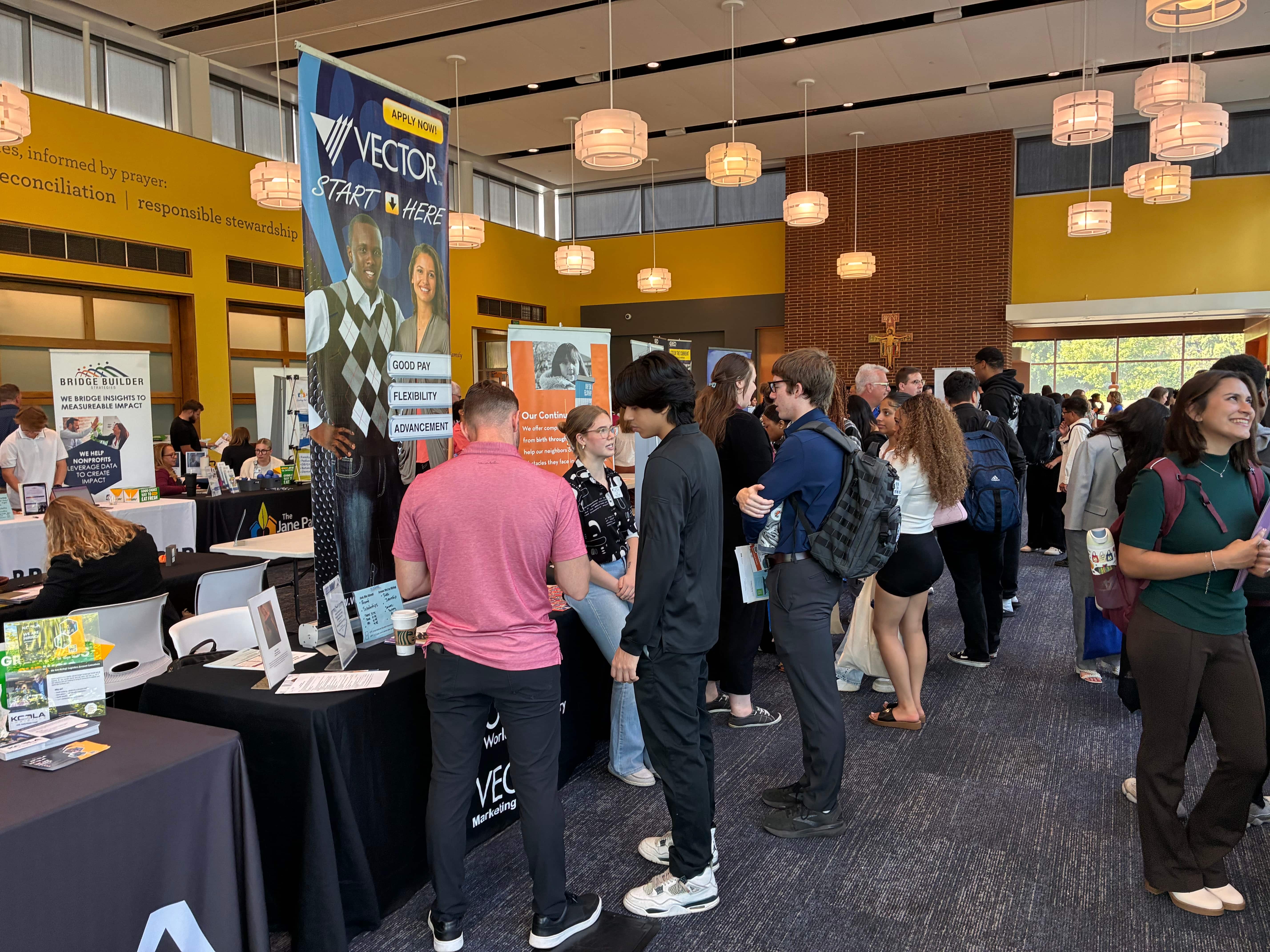 A bustling event featuring attendees engaging with various informational booths, showcasing networking opportunities and promotional materials.