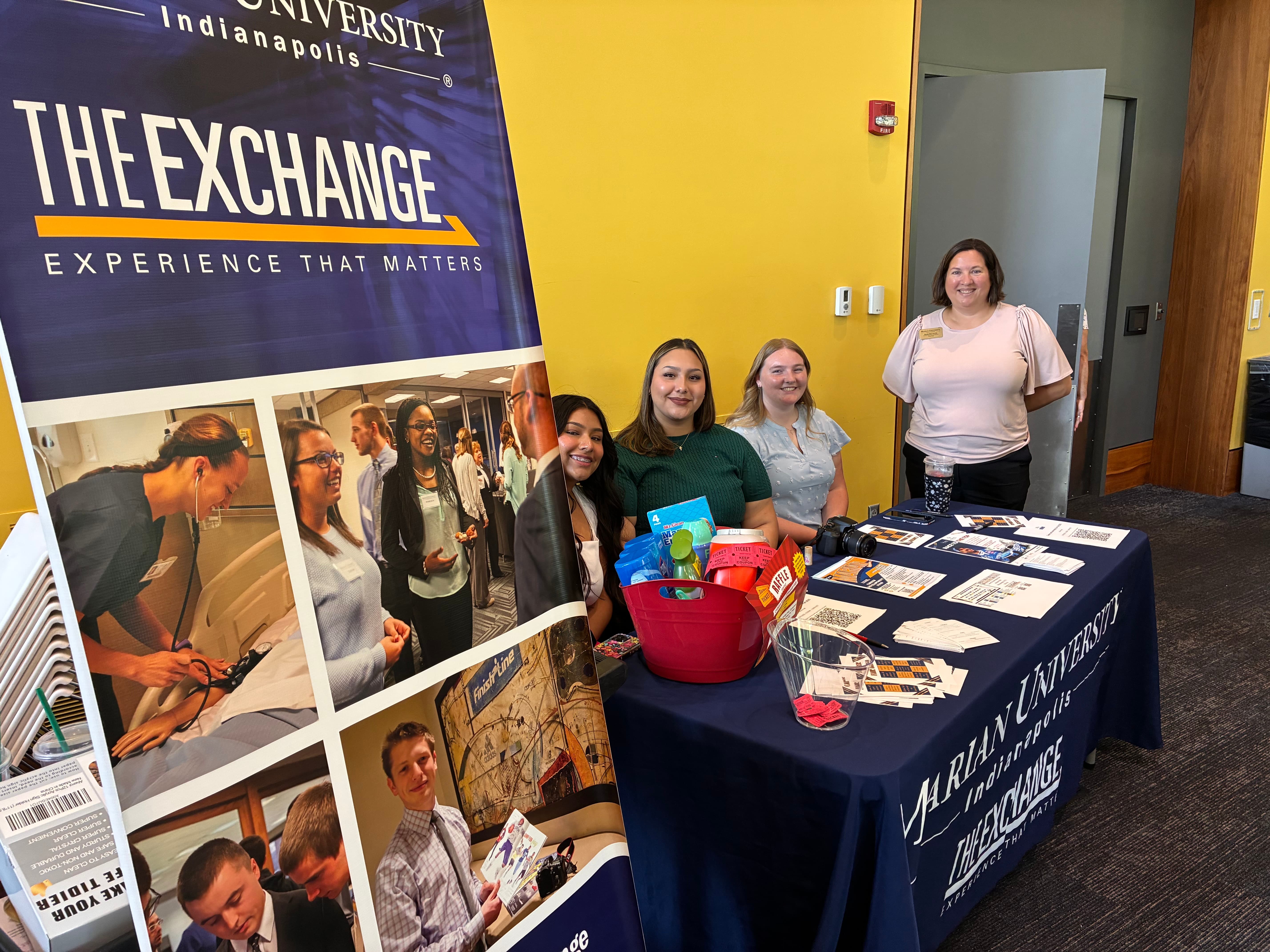Marian University representatives at a promotional booth for The Exchange, showcasing various materials and engaging with attendees.
